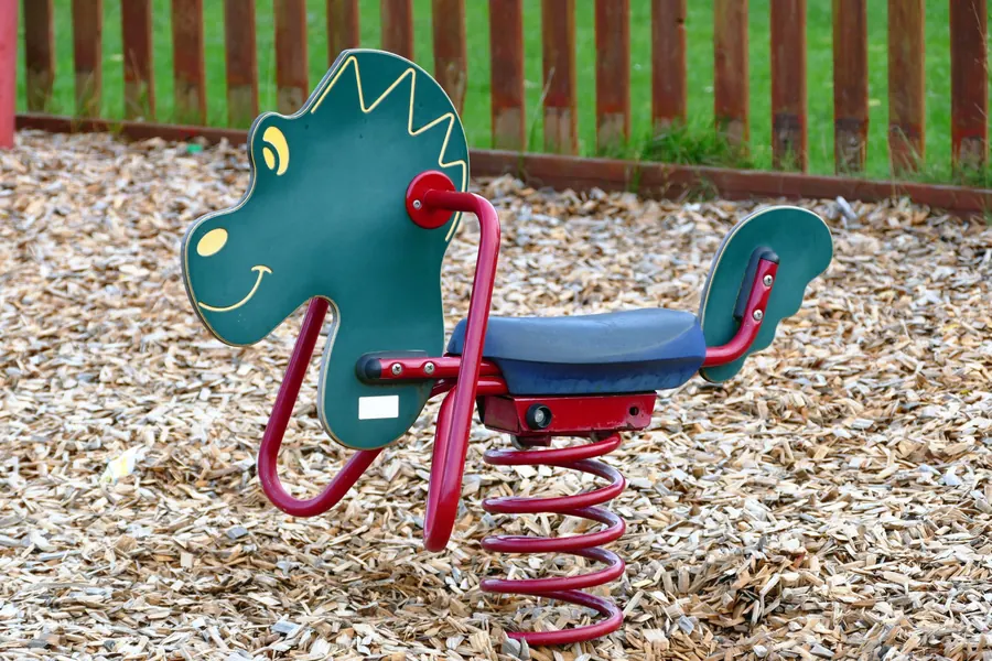 A dinosaur spring rider on soft wood-chip surfacing